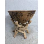 Large turned wooden bowl on wooden puzzle-style stand with carved facemasks on five splayed feet,