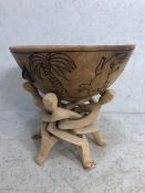 Large turned wooden bowl on wooden puzzle-style stand with carved facemasks on five splayed feet,