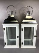Pair of modern storm lamps, white wooden frames with glass panels and polished metal tops,