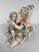 Antique Meissen figurine of 2 cherubs sat on a shoe the heel resting on a cushion crossed swords