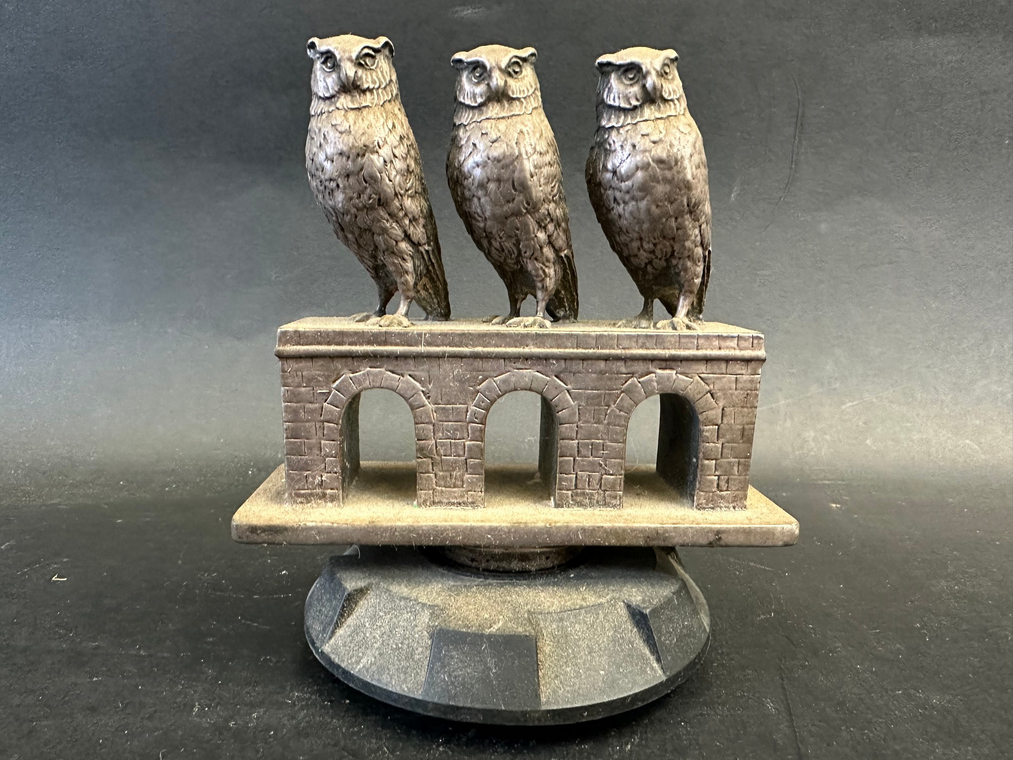A rare and unusual car accessory mascot depicting three owls evenly placed upon a bridge of three