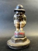 A car mascot depicting a crouching figure wearing a bowler hat, radiator cap mounted, approx. 5 1/2"