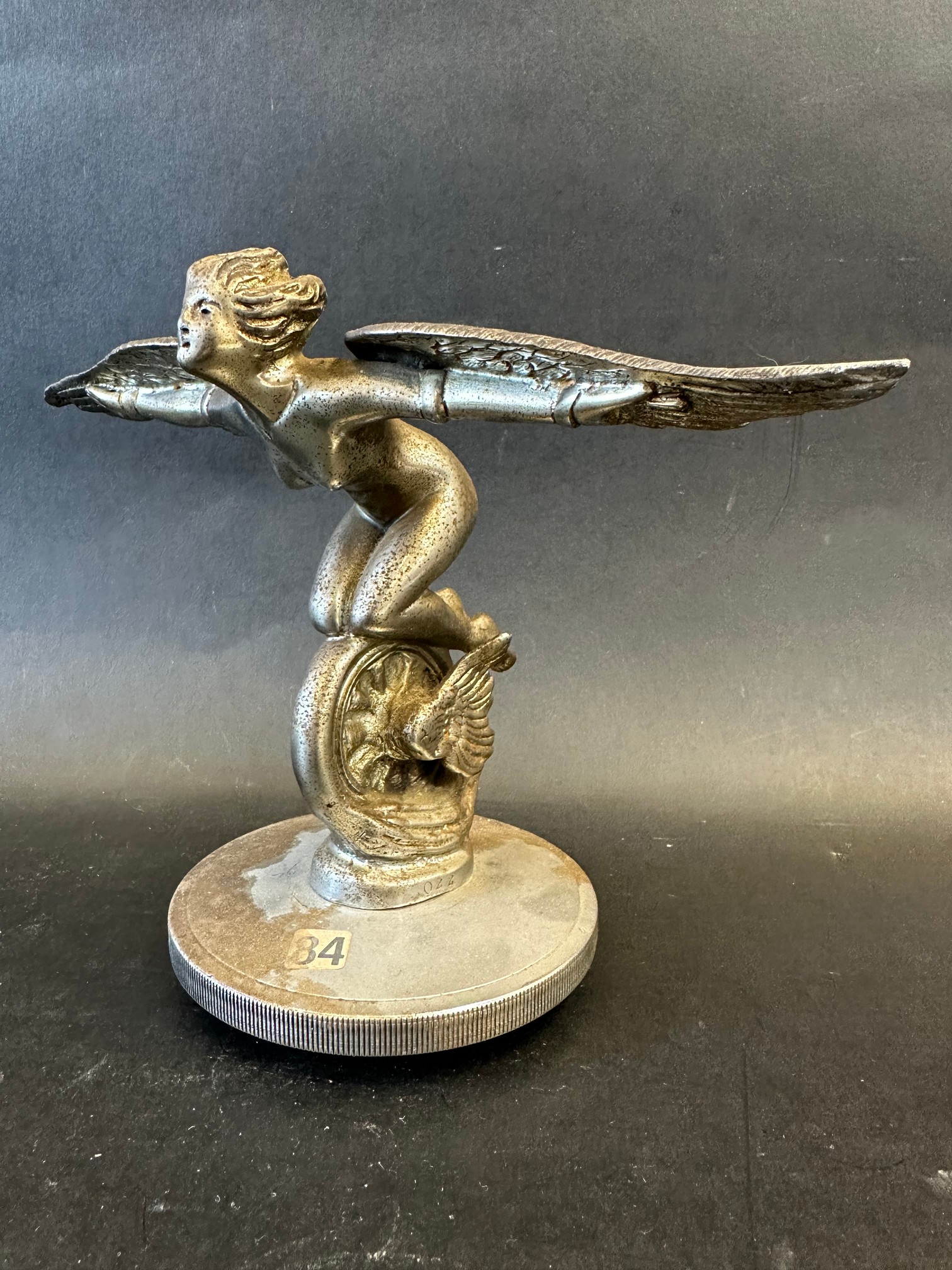 An unusual car mascot in the form of a winged speed nymph or Lady Icarus knelt on a winged wheel,