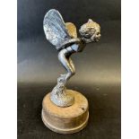 A car accessory mascot in the form of a female nude dressed with wings leaning forward upon a