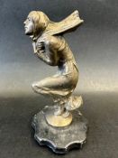 A car mascot in the form of a crouching lady clutching her wind-swept scarf, display base mounted,