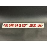 A small enamel sign bearing the words 'This door to be kept locked shut', 11 1/2 x 1 1/2".