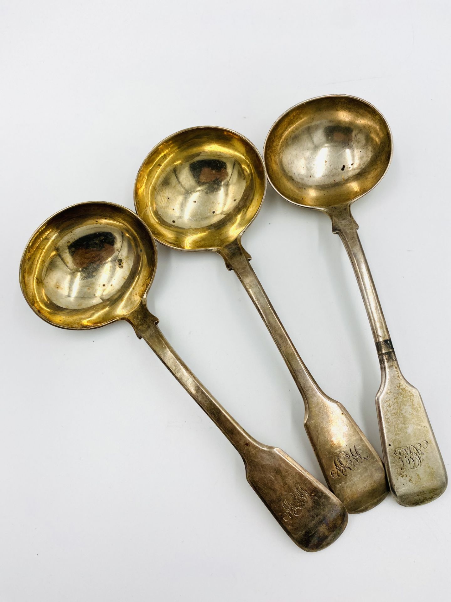 A pair of silver sauce ladles together with a silver sauce ladle