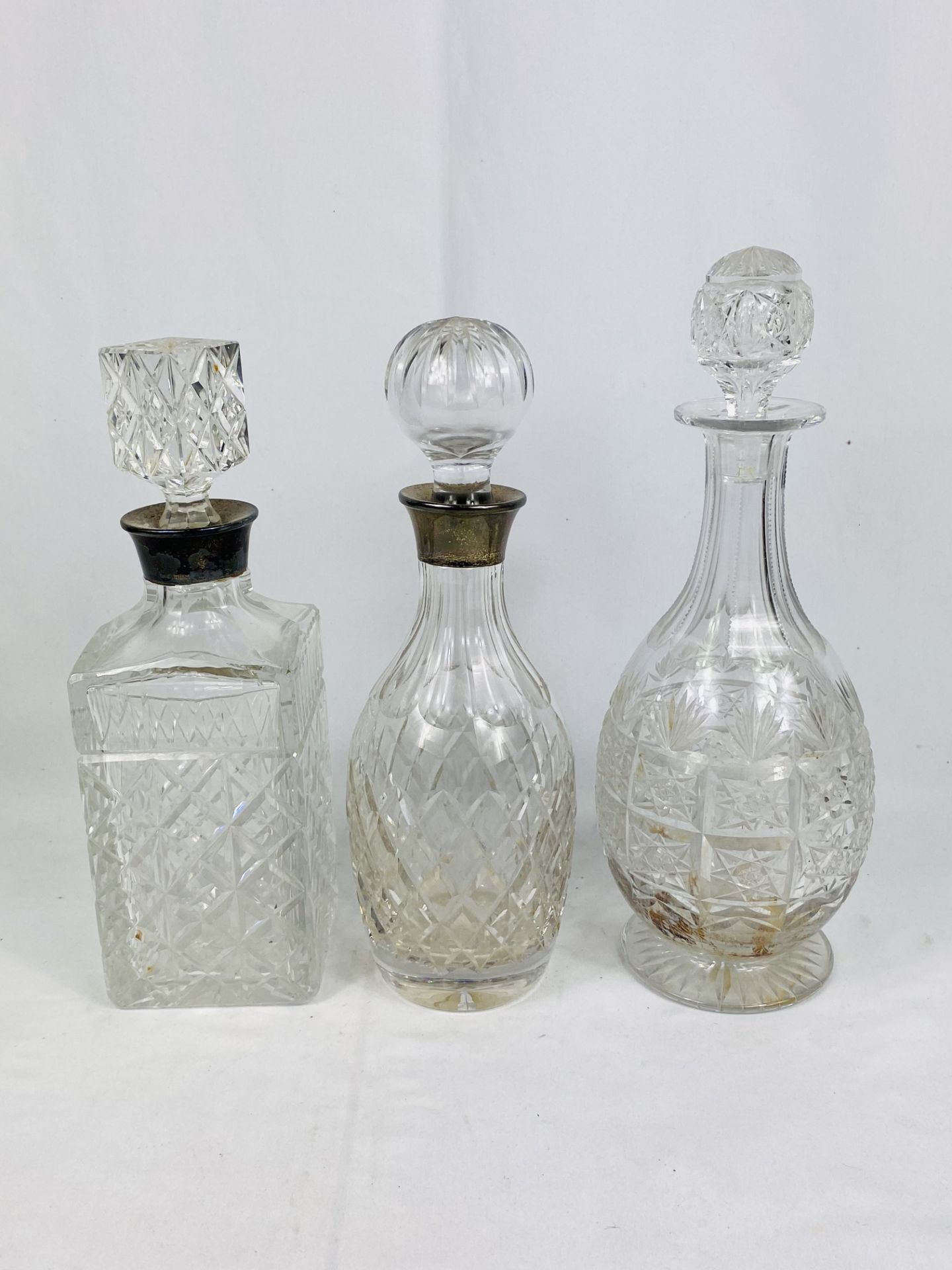 Two cut glass decanters with silver collars and a cut glass decanter