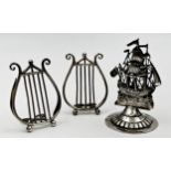 Three silver menu/card holders, a near pair of Edwardian examples fashioned as lyres, Saunders &