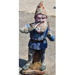 A reconstituted stone garden statue of a gnome smoking a pipe with distressed painted finish, 88cm