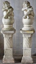 Pair of reconstituted stone cherub figures seated upon sphere cap finials, raised on column pedestal