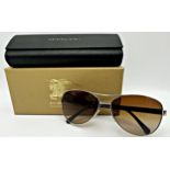 A pair of unisex aviator Burberry sunglass with a light gold frame, brown gradient lenses and