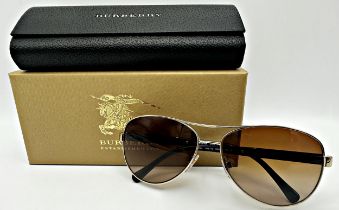 A pair of unisex aviator Burberry sunglass with a light gold frame, brown gradient lenses and