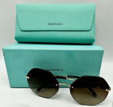 Tiffany & Co rimless hexagonal sunglasses with pale gold frame and brown gradient lenses. Model