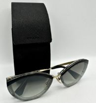 A pair of Prada cat eye shaped sunglasses with black/grey frames, grey gradient lenses and gold-tone