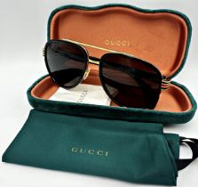 A pair of Gucci Sunglasses for men with black and gold frame and brown lenses. Model number GG0447S.