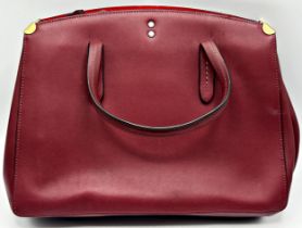 An oxblood red Coach glovetanned leather tote bag with carry handles, gold-tone hardware, internal