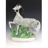 A 19th century Staffordshire pottery model of a prancing zebra, modelled wearing reigns,
