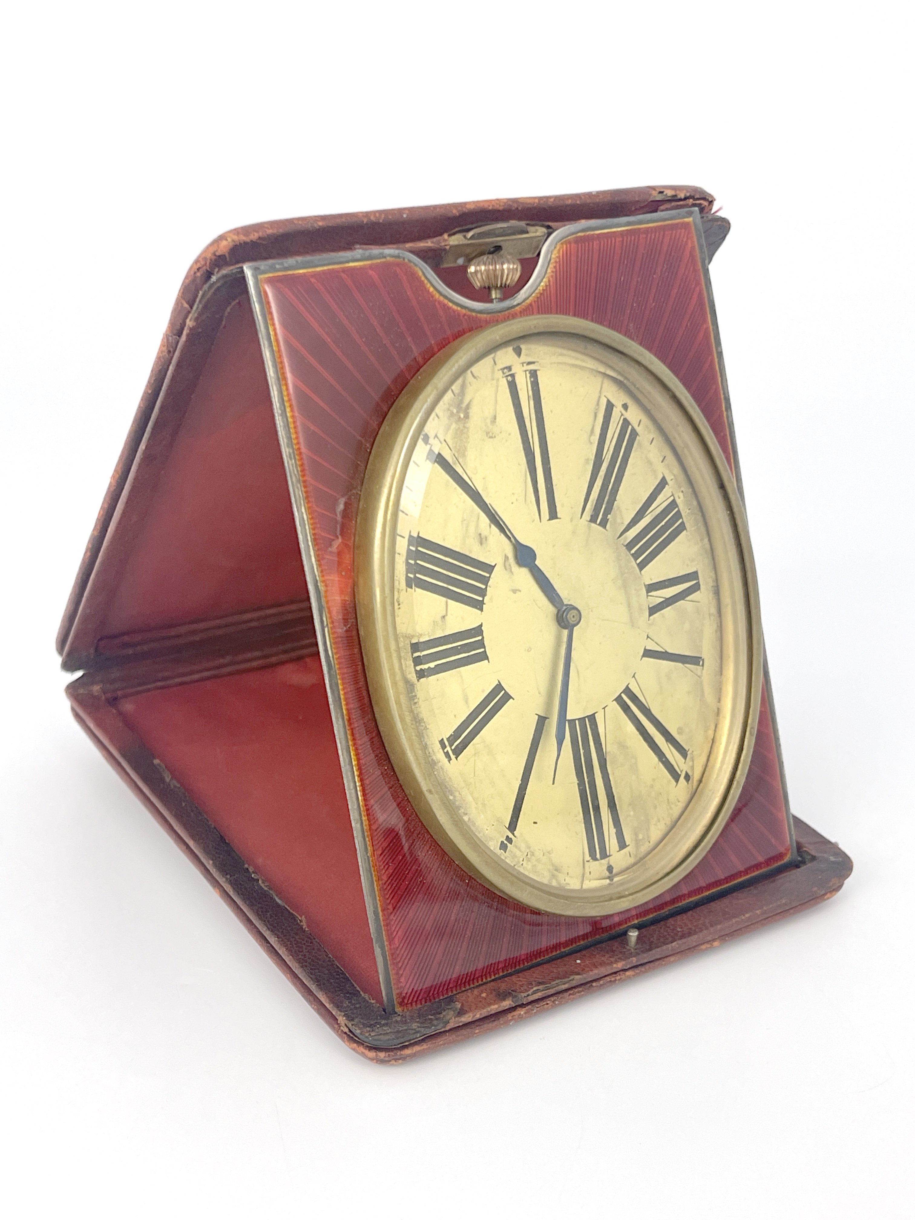 An easel travel timepiece, early 20th Century, red leather outer case, oval gilt dial with Roman