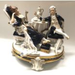 A Royal Dux figure group, taking tea, modelled as a gallant and companion seated beside a laid