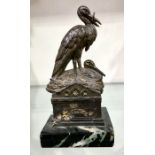 A patinated art metal figure group, modelled as nesting storks on a tomb, on marble base, 19cm high