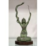 An Art Deco patinated art metal figure modelled as an Egyptian snake tamer, arms raised, on wooden