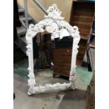 A carved wood wall mirror, white painted foliate and floral frame with foliate scroll pediment,
