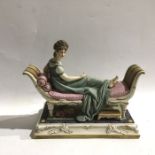 A Capodimonte bisque porcelain modelled as a lady reclining on a daybed, on square pedestal base,
