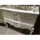 A white painted chest of three drawers, relief moulded foliage scroll decoration, on cabriole