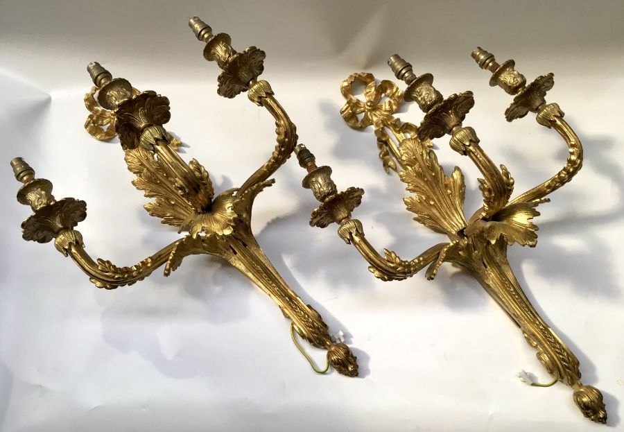 A pair of French style gilt metal three branch wall appliques, each with a ribbon crest and tapering