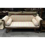 A Regency mahogany sofa, curved scroll end arms and shaped back on swept supports and brass caps and