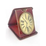 An easel travel timepiece, early 20th Century, red leather outer case, oval gilt dial with Roman