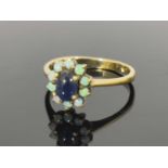 A 9ct gold sapphire and opal cluster ring, the central set oval sapphire surrounded by ten small