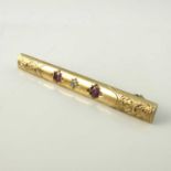 A 9 carat gold gem set bar brooch, set with rubies and diamonds, within chased foliate scrolls,