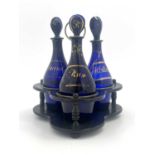Three Bristol blue and gilt glass spirit decanters in ebonised wooden stand
