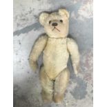 A straw-filled golden plush teddy bear, glass eyes, horizontally stitched nose, jointed limbs, cloth