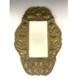 An Arts and Crafts brass mirror, in the Keswick style, ogee cartouche form, repousse embossed with