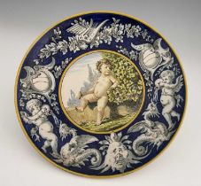 A Ginori circular faience charger, circa 1880, painted with a central roundel of a vintner cherub,