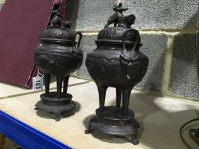 A pair of Oriental bronze koros, beast finials, twin handled vessels, tripod legs, on raised
