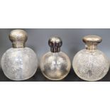 Three early 20th century glass and silver topped scent bottles, planished finish, all with glass