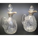 A near pair of Arts and Crafts William Comyns silver topper glass jugs, the bodies with etched