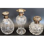 Three Edwardian silver and glass scent bottles by William Comyns, embossed lids depicting angels and