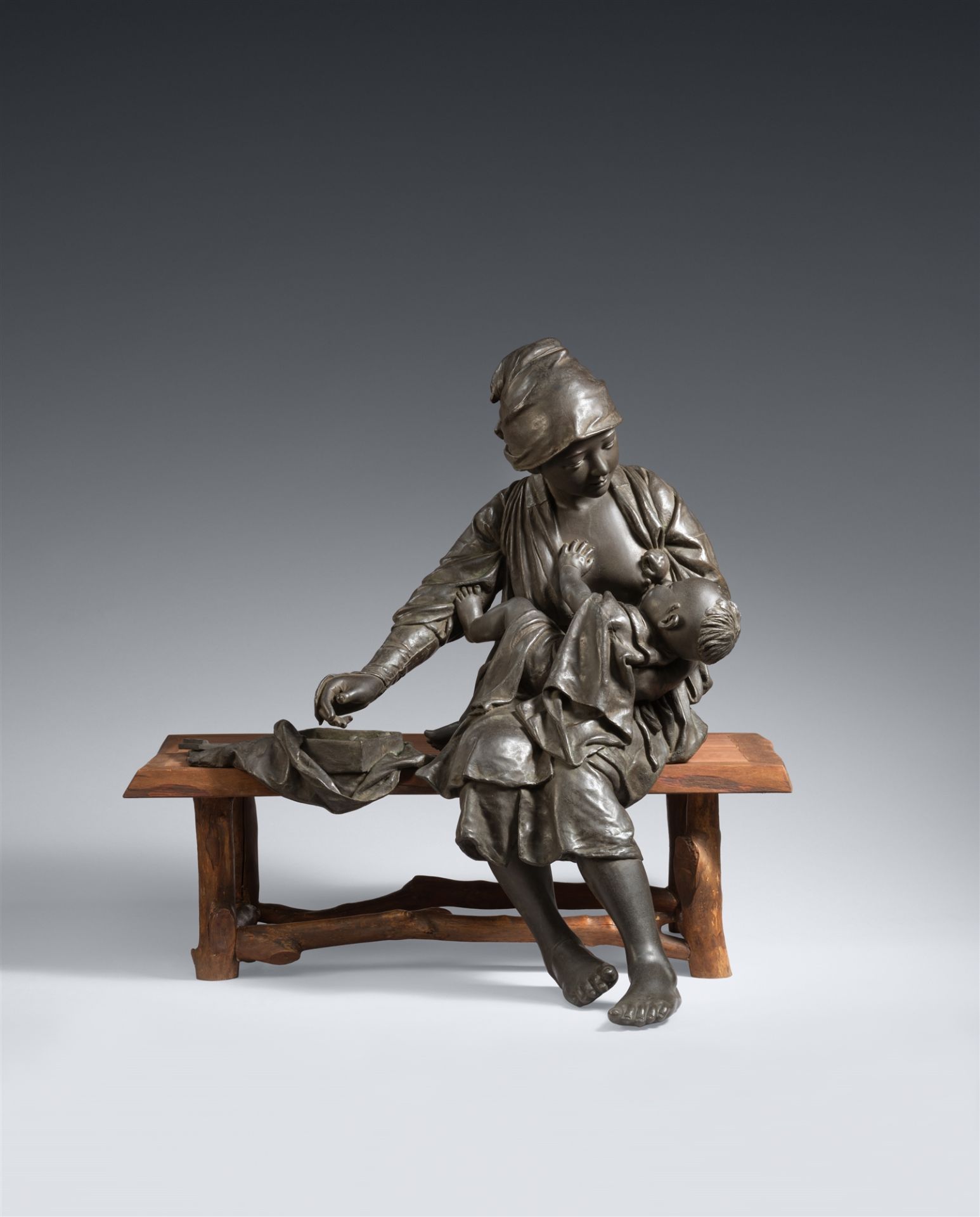 An Udagawa Kazuo cast bronze figure of a young mother with her child, seated on a wooden bench. Toky