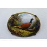 Painted oval porcelain brooch depicting pheasants in the woodland, signed R Hague, possibly for