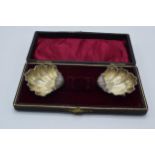 A cased pair of silver shell salt dishes in velvet and fabric lined case, 15.0 grams.
