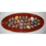 A collection of hard stone eggs in a modern bamboo-style dish, 60cm long (30 eggs). Collection