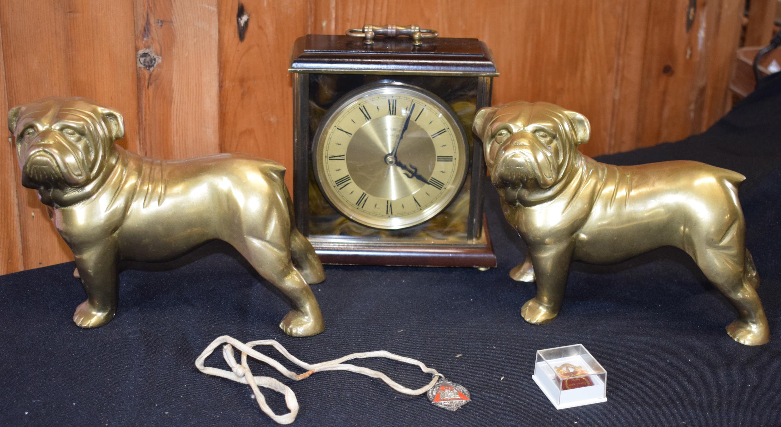 A pair of cast brass bulldog figures together with a mantle clock and 2 enamelled badges.