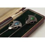 Cased pair of Art Nouveau hat pins with enamelled decoration and hammered Liberty style elements,