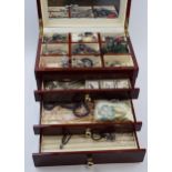A modern wooden jewellery case with folding lid and pull out drawers with a collection of costume