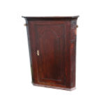 A George III oak hanging corner cupboard - the arched panel door enclosing a pink painted interior